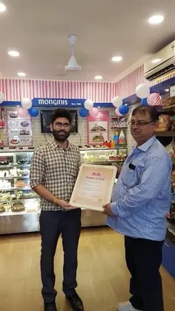 Two men holding a certificate inside a Monginis cake shop
